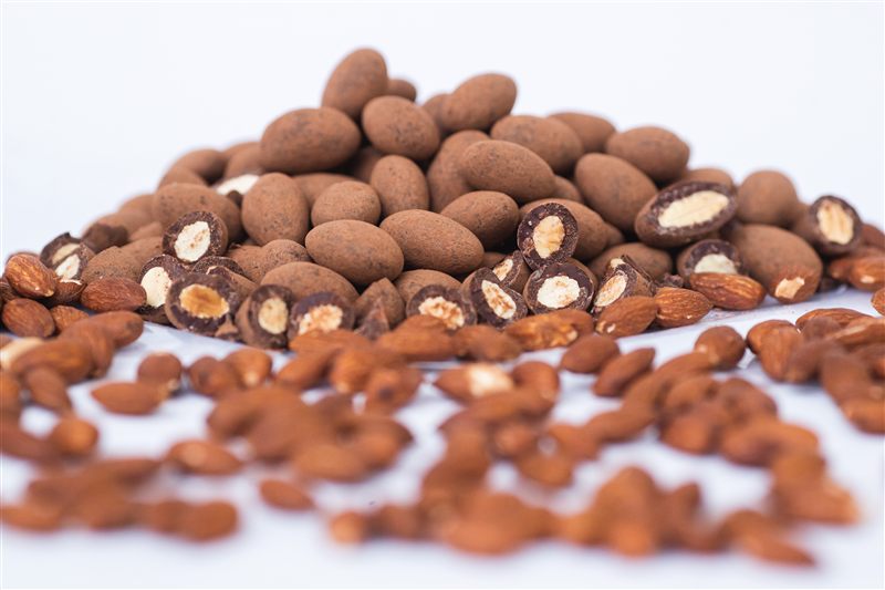 Drageados de amêndoa cortados ao meio mostrando a castanha por dentro, com amêndoas cruas ao redor